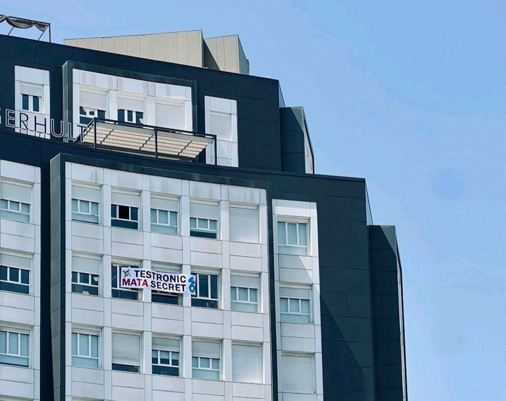 Foto del exterior de un edificio, del que cuelga una pancarta que dice "Testronic mata Secret6 Madrid"