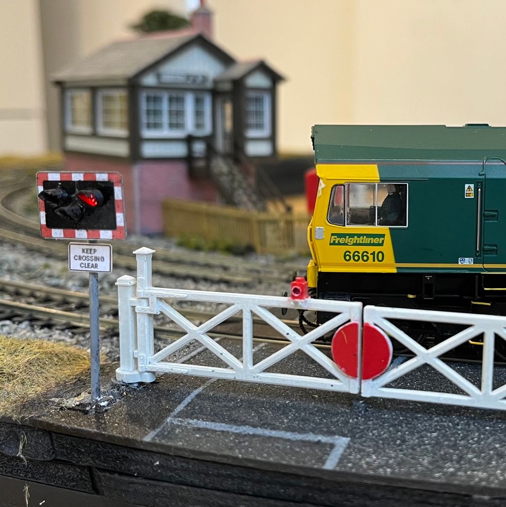 Model railway level crossing with illuminated signs and freight locomotive. 