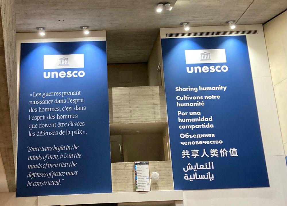 Banners hanging at UNESCO. One reads “since wars begin in the minds of men it is in the minds of men that the defenses of peace must begin. The other reads (in multiple languages) Sharing humanity 