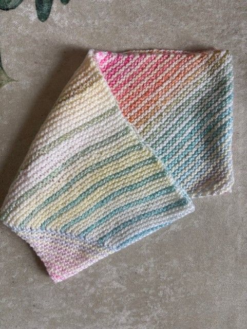 A cowl with alternating white/yellow and pastel gradient yarns. It's folded over on itself. The top section shows varying wider stripes of white/yellow, with green and blue pastel 1-row stripes between. The bottom section shows bias 1:1 stripes.
