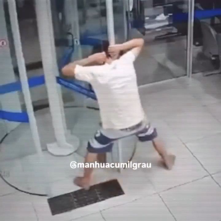 Um cara preso com a cabeça numa porta de vidro giratória de banco