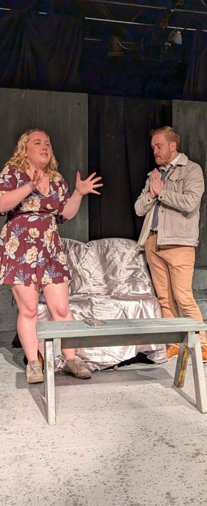 Image of Jake looking intense and annoyed as a woman gestures next to him. He is on a stage set 