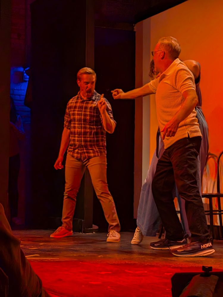Picture of Jake on stage angrily pointing and shouting at a man in white 