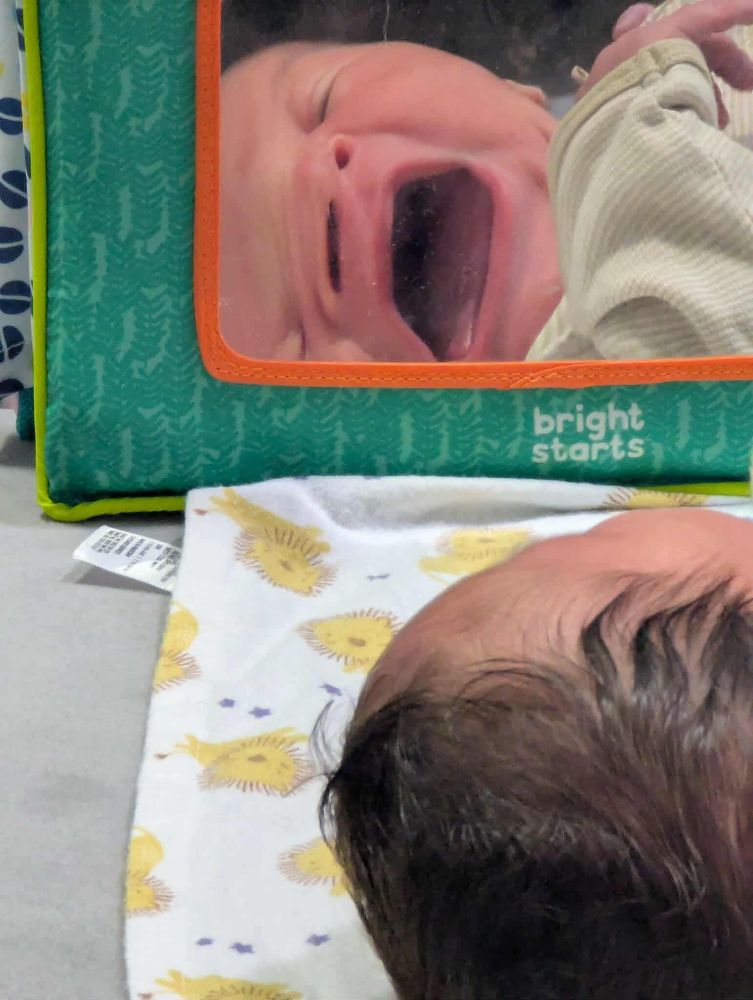 A baby staring at a very distorted reflection.