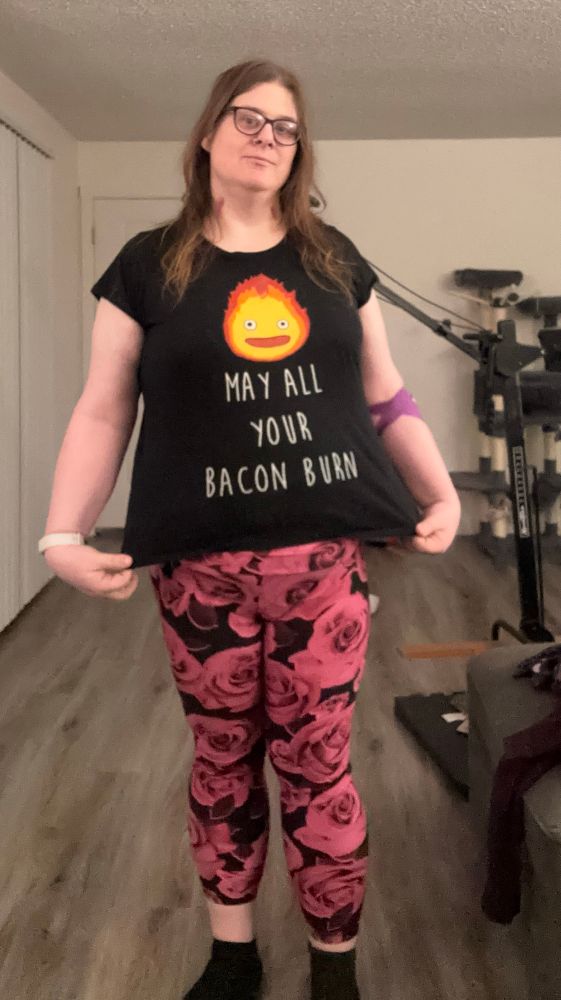 A picture of Zoe wearing her Calcifer shirt with the text “May All Your Bacon Burn”