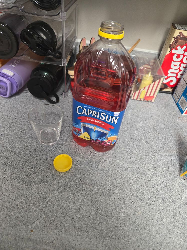An opened jug of Capri Sun Fruit Punch sitting on a counter next to a small glass.