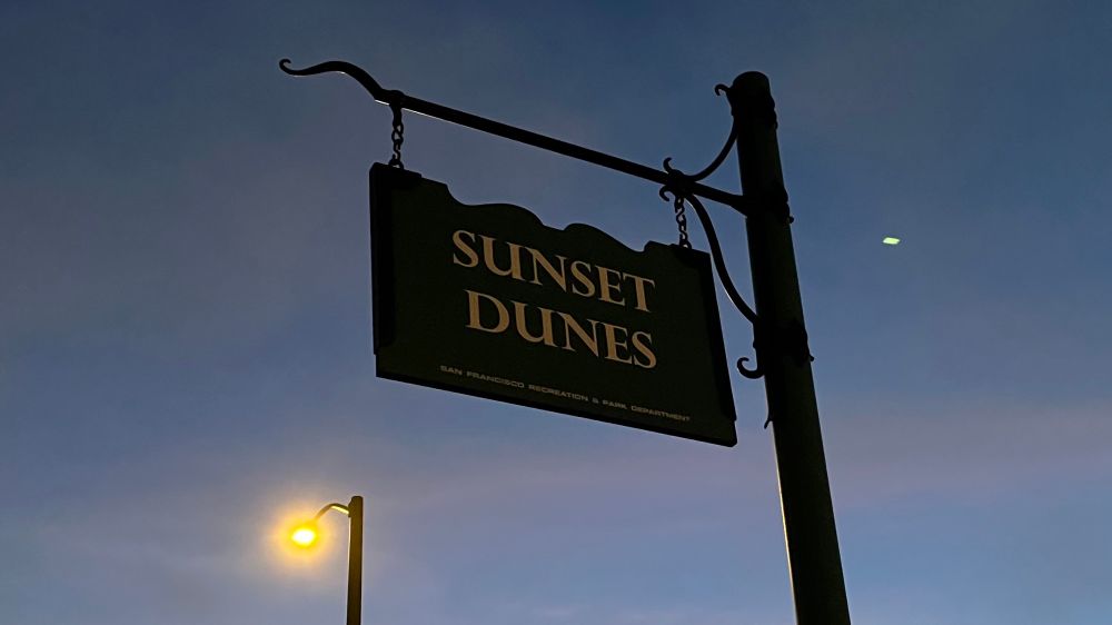 a park sign that says SUNSET DUNES before a twilit sky