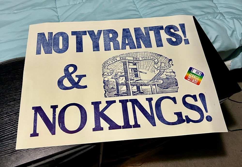 a large poster on off-white paper with blue ink that says, No Tyrants and No Kings, with an image of a wooden printing press with a banner above it that says, The Tyrants Foe, The Peoples Friend. resting on top is a small sticker of a rainbow floppy disk that says Skeuomorph Press