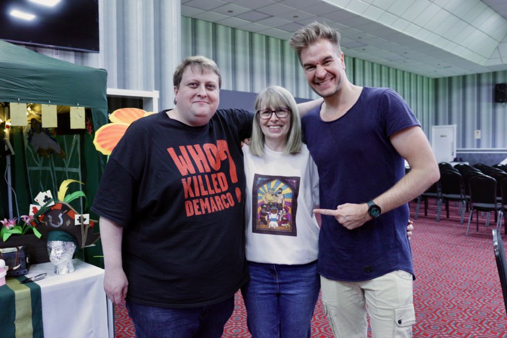 Loki, Liz and Leator in the SoTFest avenue. Liz stands in the middle, wearing a shirt showing a painting in style of stained glass with Blairs, Cats and Liz pirates kneeing before Saint Lokis and Saint Leators pirates