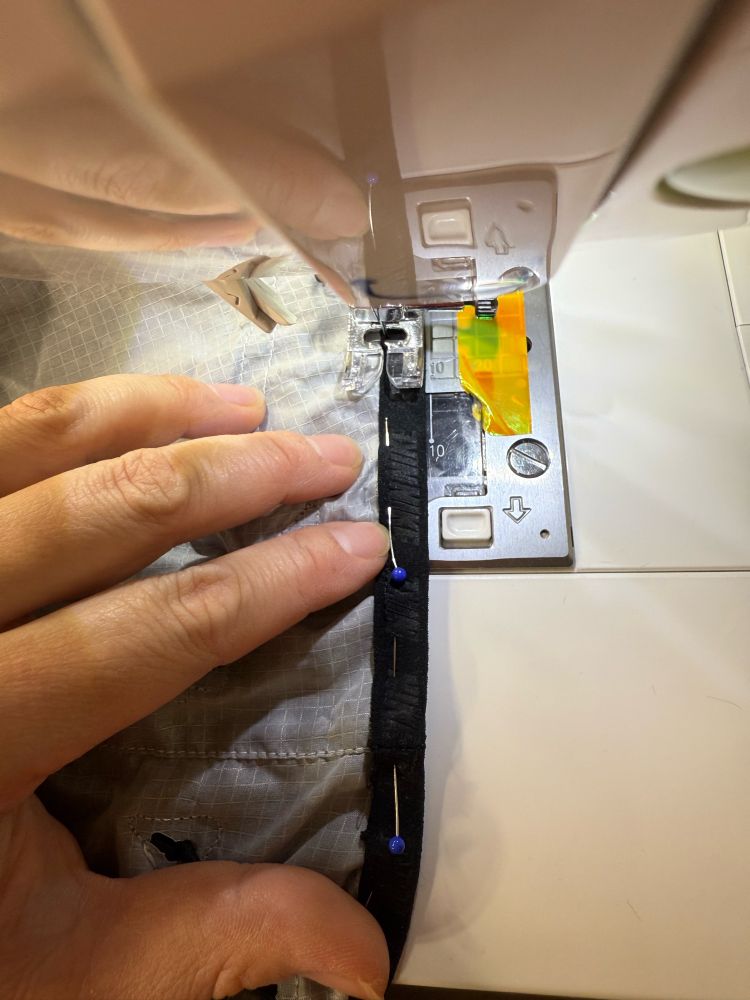 Close up of black Nike logo binding being sewn back onto a white poncho, held in place by pins 