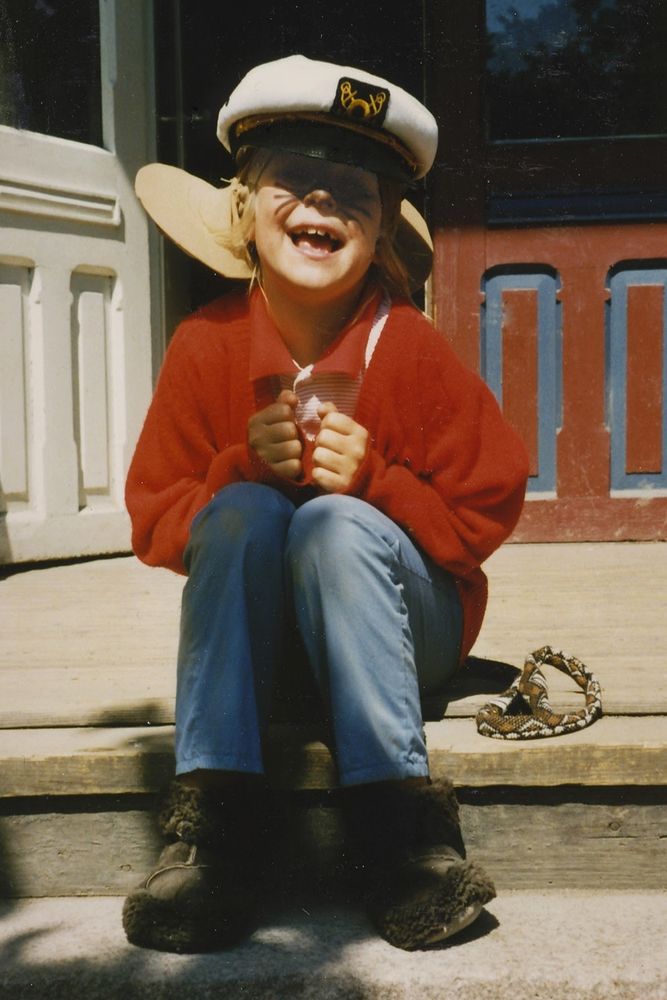 Rin as a child, dressed up as Fivel from the movie An American Tail, and sitting on the stairs in front of their kindergarten, looking very happy.