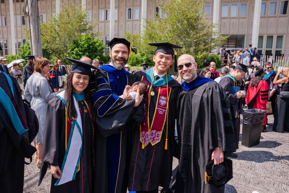 Two proud professors, two happy students, and a sleepy baby in academic regalia at graduation.  