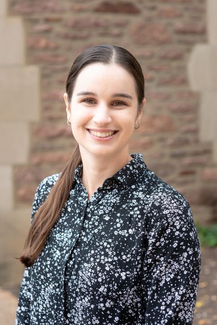 Rachel Smith Peirce has long brown hair and is wearing a black button-down shirt with small white flowers.