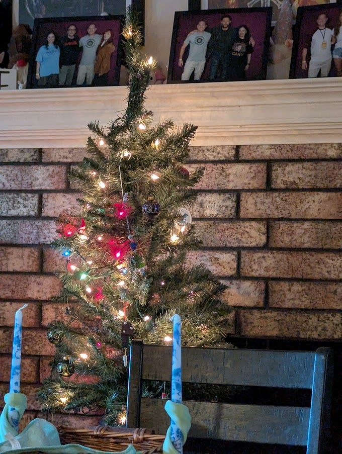 A photo of a small christmas tree with multi-colored lights. In front of the tree are two aqua colored candle stick holders with white and blue candles in them. There are ornaments on the tree, but you really can't see them.