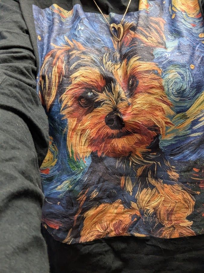 A photo of a long sleeve black shirt with a graphic. The graphic is a painted brown and black yorkipoo with a Starry Night inspired background.