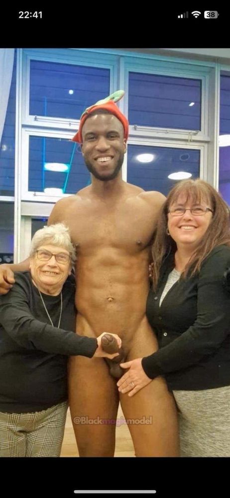 Old lady holding the erect penis of a tall black male stripper from the UK Pleasure Boys group. There's another lady with her hand close to his scrotum. The three of them are smiling at the camera.