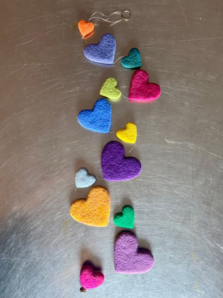 A string of multi coloured and sized needle felted hearts on a stainless steel table top
