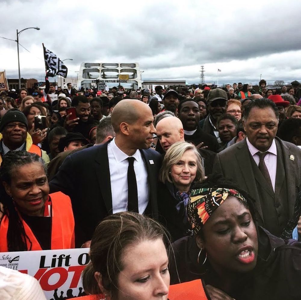 Hillary Clinton in a crowd marching across the Edmund Pettus Bridge, flanked by Cory Booker and Jesse Jackson