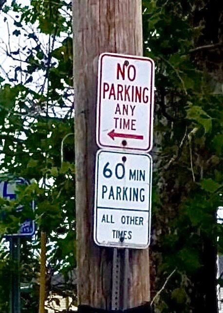 Street signs: the top one says “no parking any time” with an arrow pointing to the left / the bottom one says “60 min parking all other times”