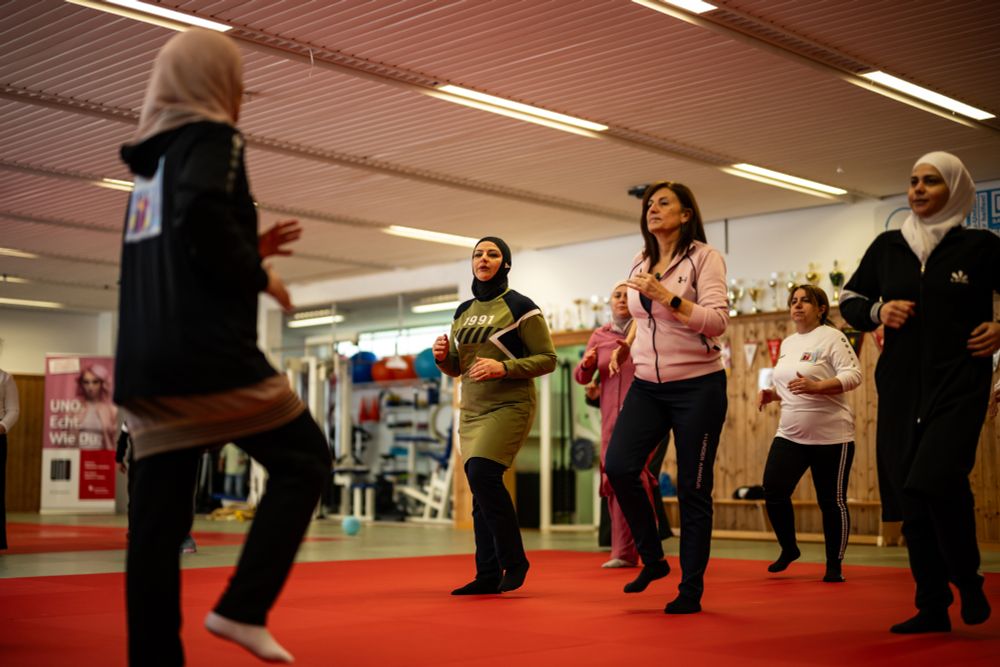 Sportlerinnen bewegen sich in einem kleinen Turnraum. Drei Sportlerinnen tragen einen Hijab. 