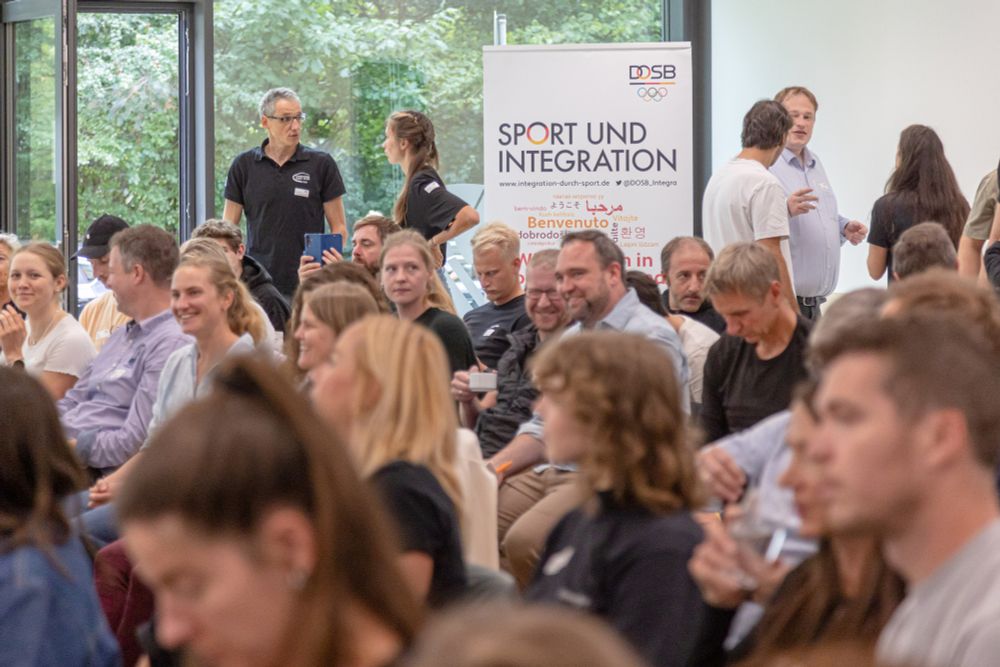 Die Teilnehmenden des Fachforums sammeln sich im Plenum und sitzen vor einem Banner im Austausch.