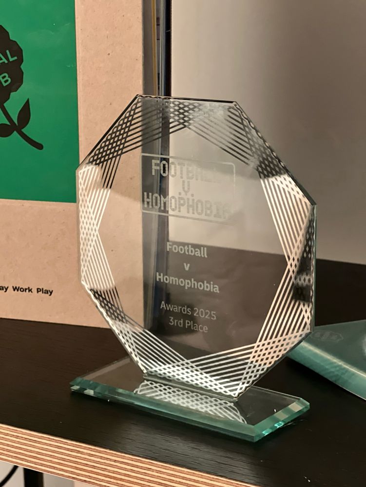 An octagonal glass trophy on a shelf with the words “Football v Homophobia Awards 2025 Third place”written on