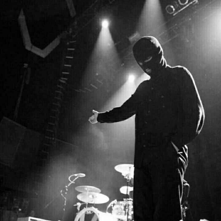 Tyler Joseph wearing a black balaclava looking down and pointing his arm to the side with finger guns. He’s on stage during one of the earlier shows, more so during the Blurryface era I thing around 2015/2016.