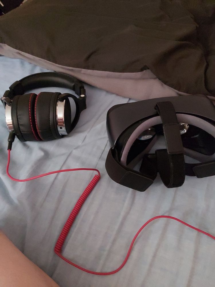 A black vr headset and chunky black headphones resting on a bed