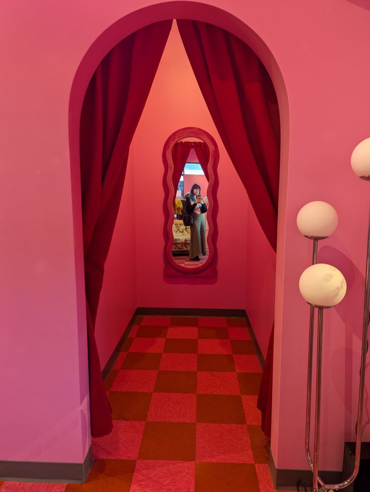 Pink and red checkered floor. Pink walls, red drapes, mirror in a changing room. 