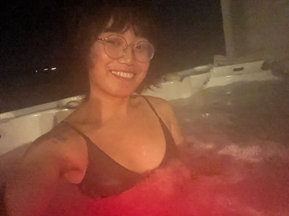 A girl (me) taking a selfie while in a hot tub. In the picture, I’m wearing a black bikini. 