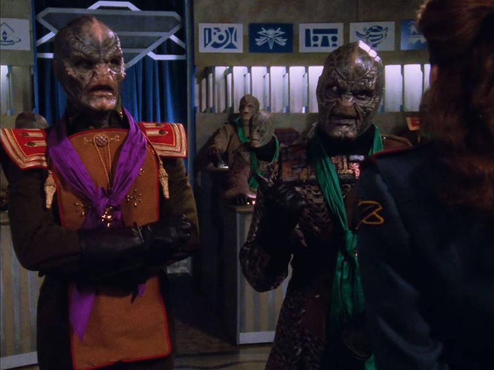 Two aliens of the same race arguing with a women. They are wearing scarves, left is purple, right is green. Context: they are a race at war and they kill each other depending on the color of the scarf 