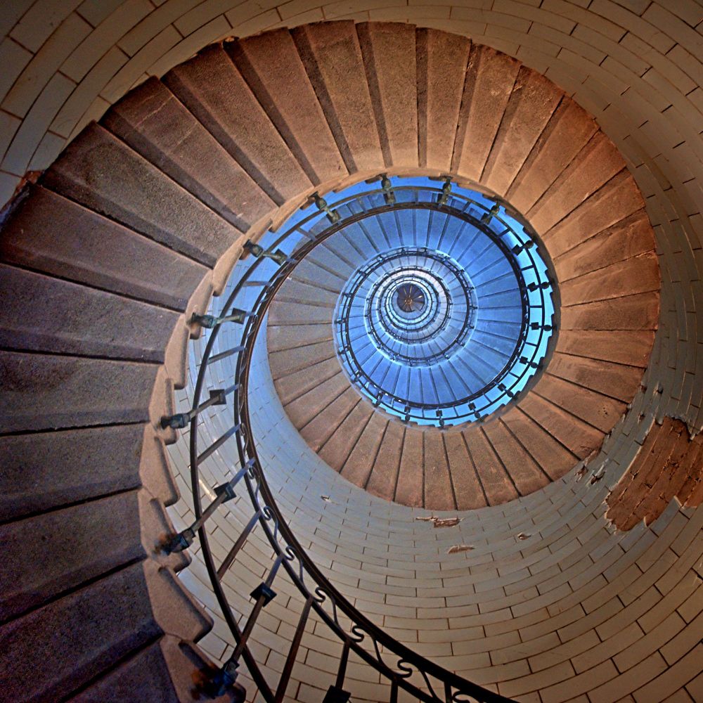 Wendeltreppe im Leuchtturm,  von unten fotografiert.  Spiralmuster, Farbverlauf von hellbraun außen zu hellblau Richtung Mitte.