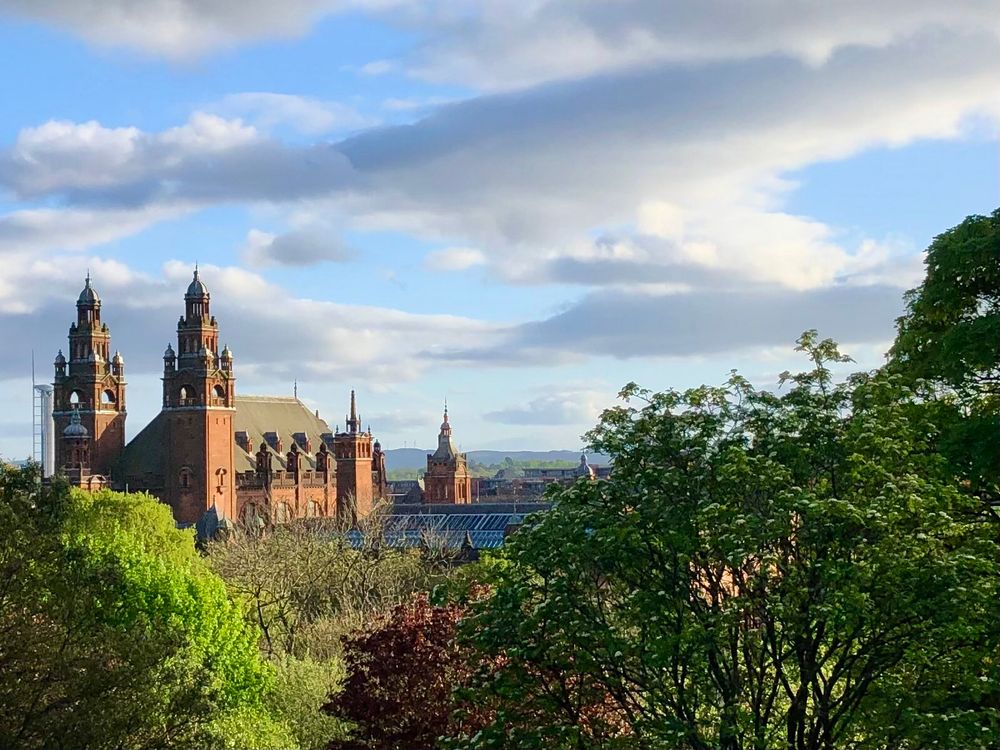 Redbrick neogothic building in glorious evening light with trees and shrubs in the foreground 