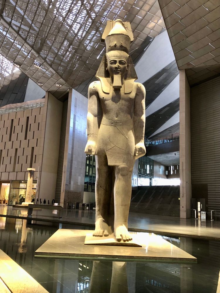 Large statue of King Ramses in the huge, light and airy hall of the Grand Egyptian Museum. Looks golden in the evening light coming through the glass pitched roof