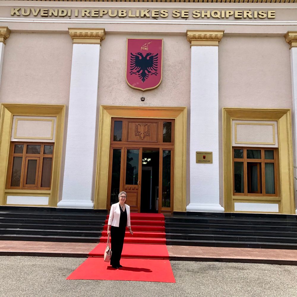Woman standing outside main entrance of a building with national emblem above door - a black double-headed eagle on a red background 