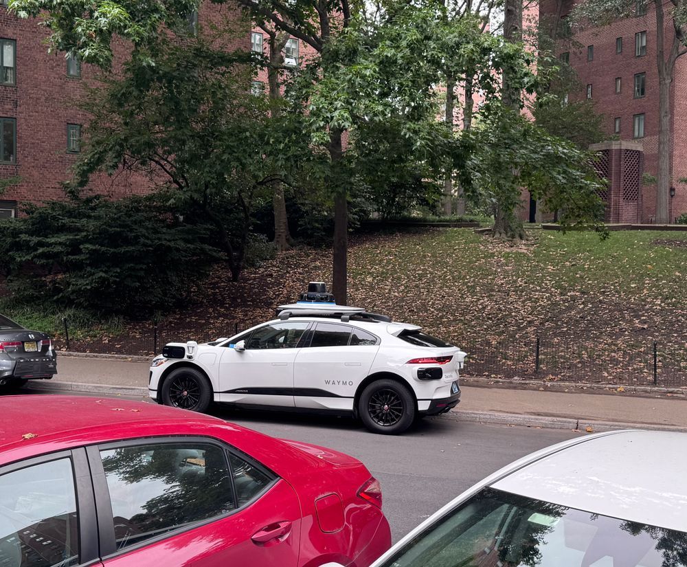 A Waymo-branded self-driving car parked on a side street in front of a tree.