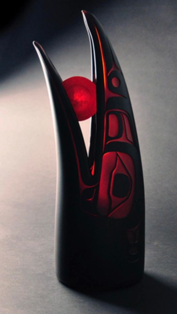 scultpure d'une tête de corbeau en cristal noir et rouge translucide
dans son bec une boule rouge