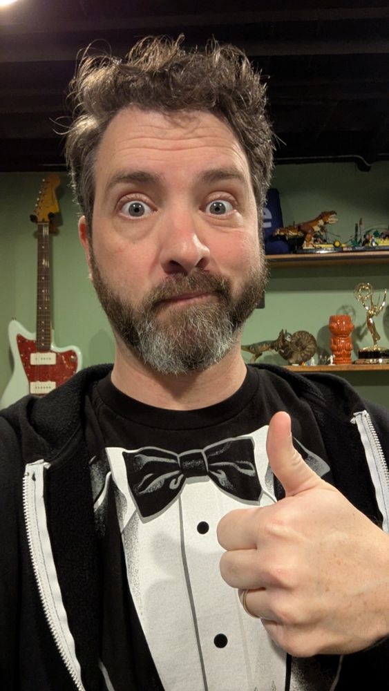 Kyle wearing a tuxedo T-shirt, looking vaguely excited