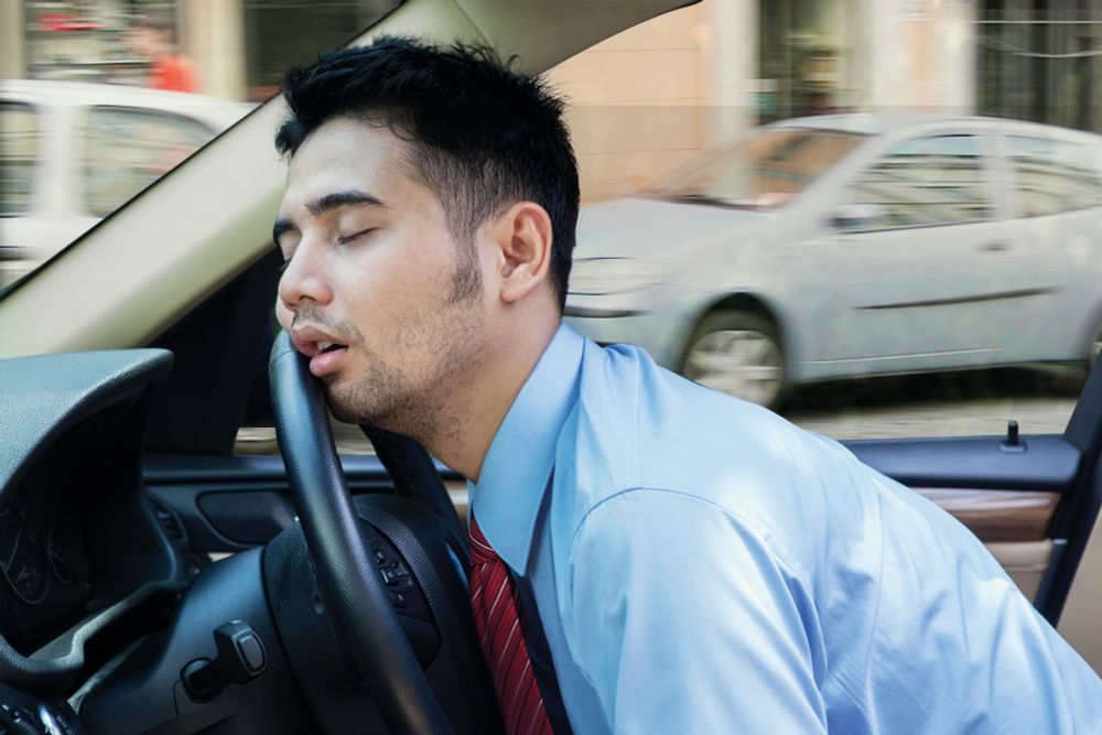 Man in shirt sleeping against the steering wheel of a car. 