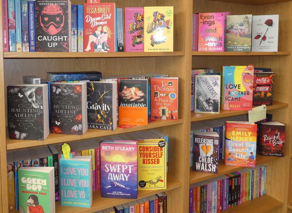 Photo of part of our romantic fiction section with various books facing forward - Haunting and Hunting Adeline, new Beth O'leary, Emily Henry and other hardbacks, new Navessa Allen, Tessa Bailey, Emet North paperbacks. More shelves out of shot below, more books in YA, SFF and elsewhere!