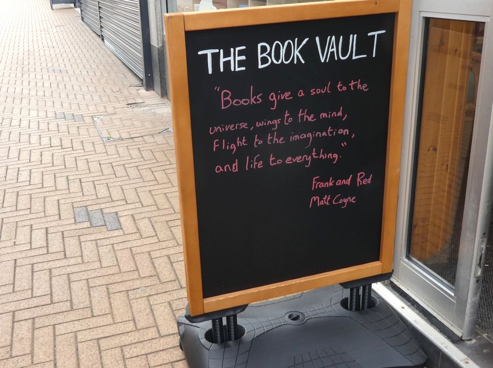 Pavement blackboard, The Book Vault in white writing at the top (we will do a more arty thing when time allows!), and a quote - Books give a soul to the universe, wings to the mind, flight to the imagination, and life to everything. A quote from a character in Frank and Red, by Matt Coyne.