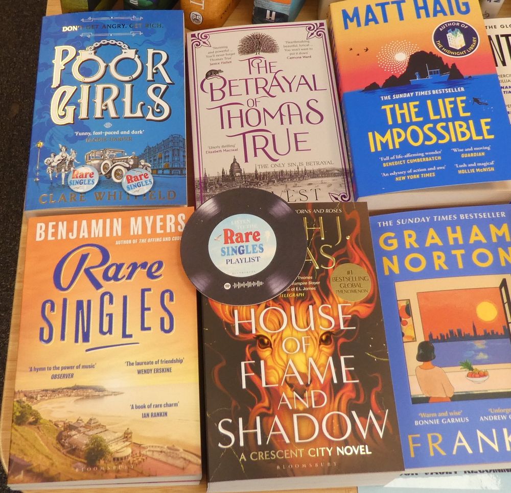 Photo of books, focus on the new paperback edition of Rare Singeles from Benjamin Myers, with a couple of small badges and a Rare Singles mugmat in the design of a record. Left over from the hardback release just a couple of freebies available! Also in shot Sarah Maas House of Flame and Shadow, A J West The Betrayal of Thomas True, and Poor Girls from Clare Whitfield, all new-release paperbacks.
