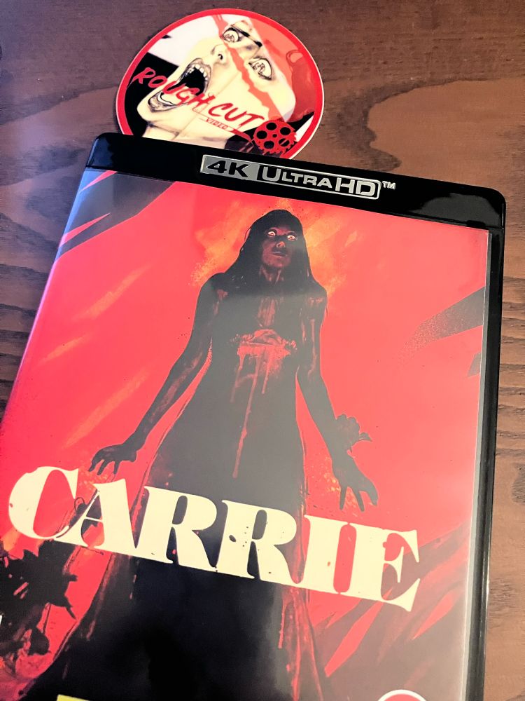 Photo of the front cover of a blu-ray dvd of the classic horror movie Carrie. A scared looking teenager in a dress against a red backdrop.