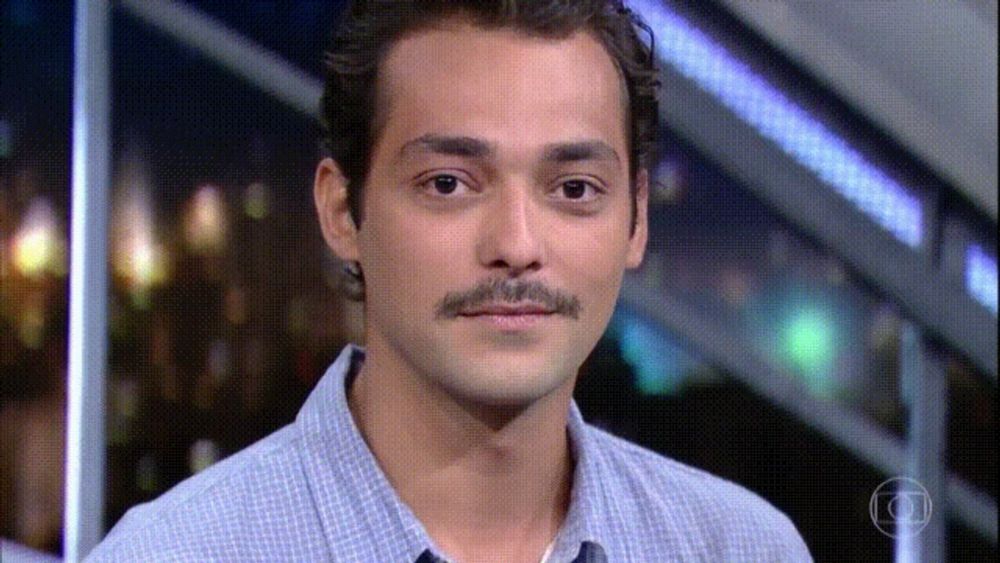 a man with a mustache looks at the camera with a blurry background