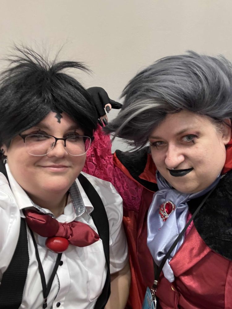 A selfie of two white people, one cosplaying Blitzø and the other cosplaying Stolas from the YouTube animation Helluva Boss