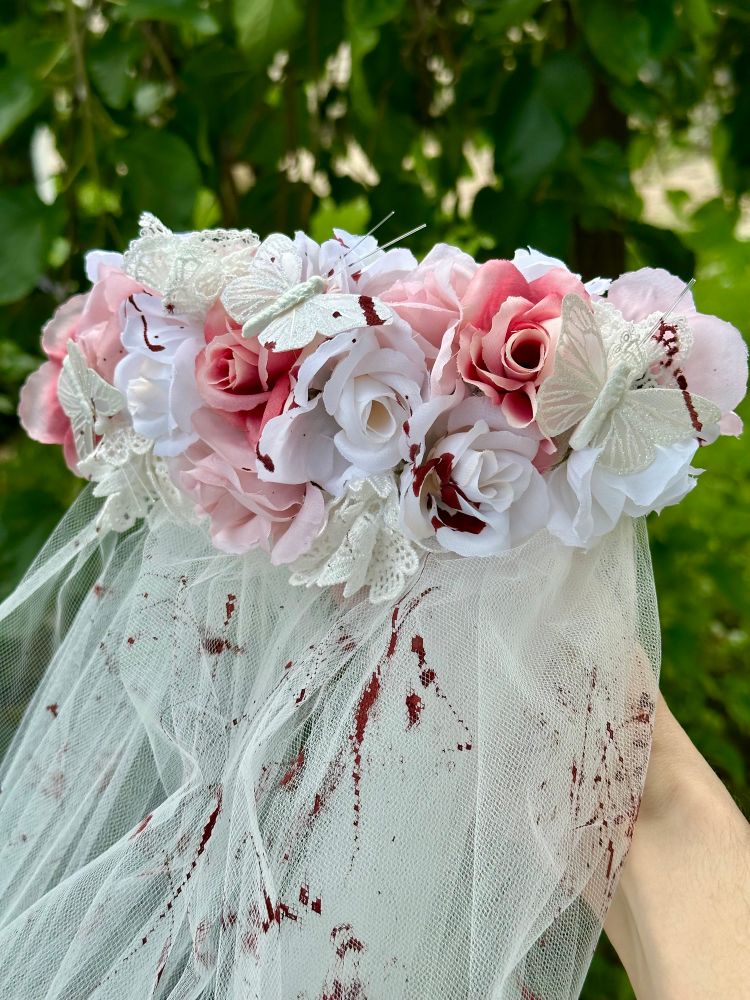 A hair clip with roses and butterflies above a veil, spattered with “blood”
