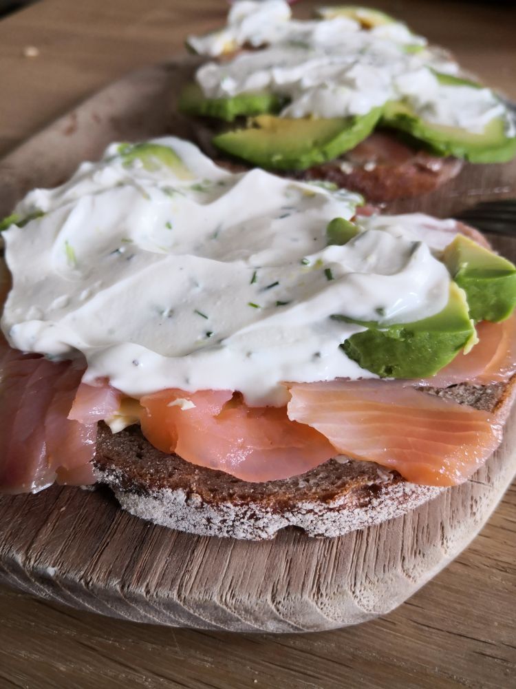2 belegte Brote mit Lachs, Avocado, Schnittlauchquark, auf einem Holzbrett. Nahaufnahme