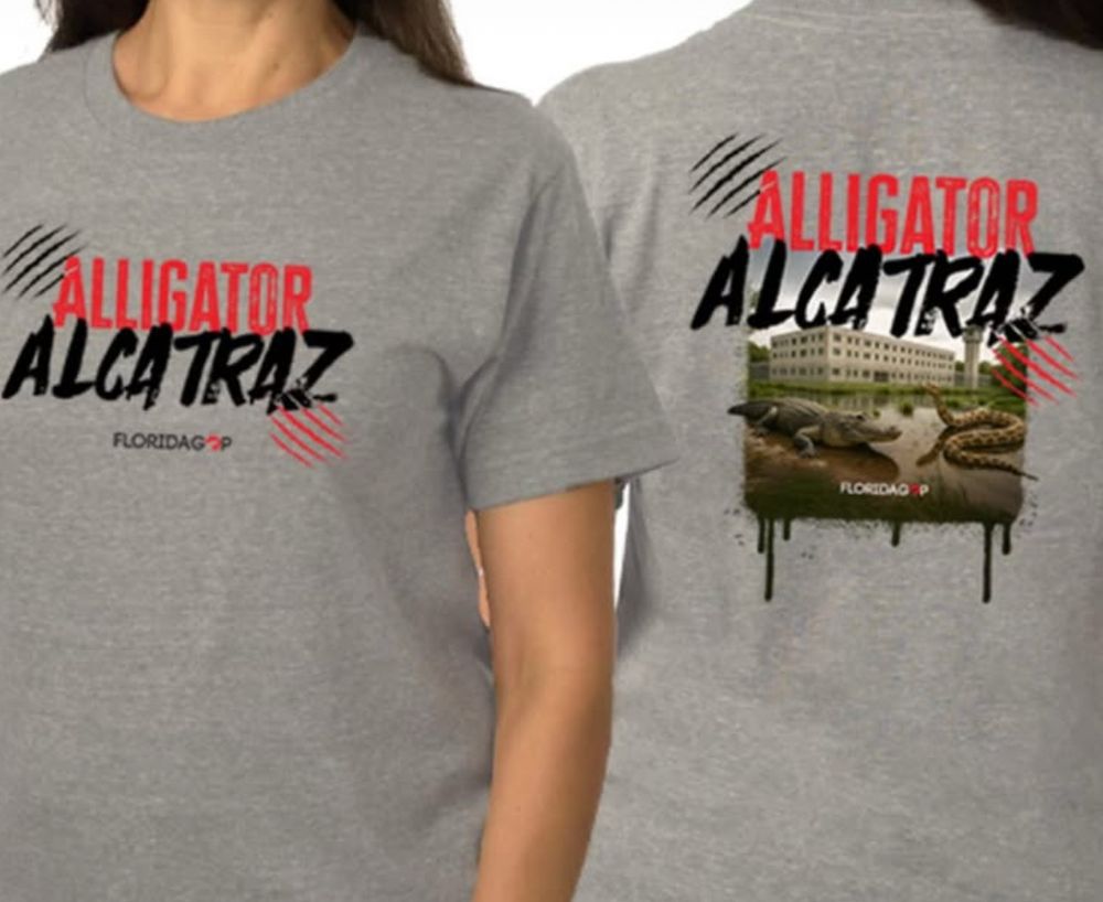 A screenshot of the grey t-shirt that says "alligator alcatraz" and features an ai slop image of an alligator and a large snake in front of a prison