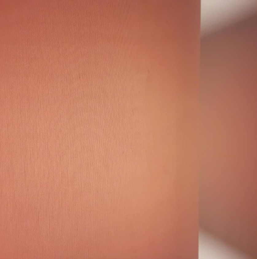 Close-up of a textured, peach-colored wall with soft lighting and a blurred reflection on the right side.