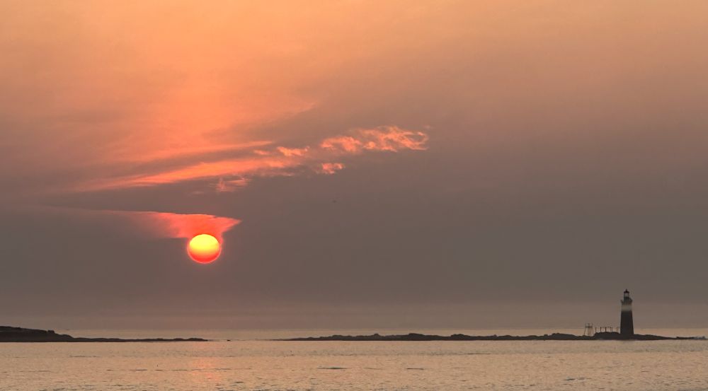sun rise over ocean with lighthouse in the foreground. 